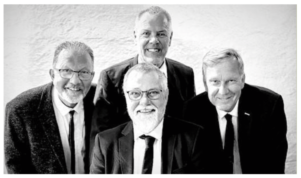 Fire mænd i jakkesæt smiler til kameraet