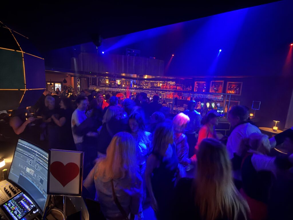 Fyldt natklub med dansende gæster og DJ-pult